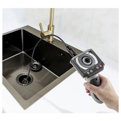 Hand holding a inspection camera aimed into a kitchen sink drain and garbage disposal, showing plumbing inspection or cleaning use.