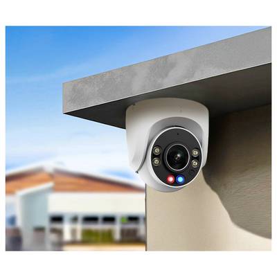 Security camera mounted on a building corner, overlooking a parking lot. Bright sky and blurred building in the background.