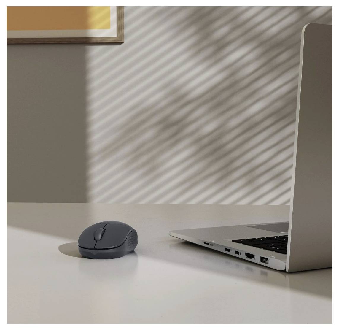 'A laptop and a wireless mouse on a sunlit desk, with shadows from blinds creating patterns on the wall.'