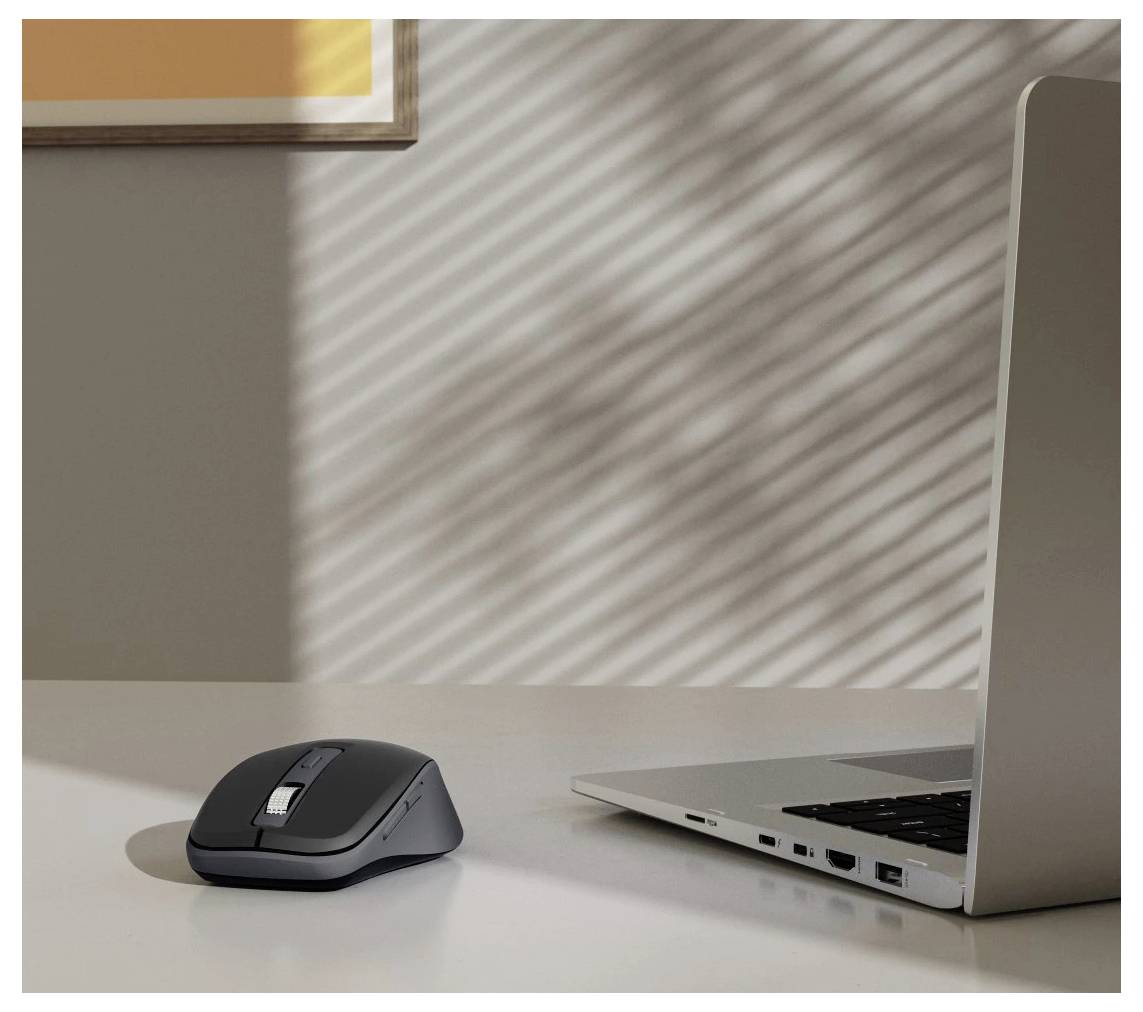 A silver laptop and a black wireless mouse on a white desk, with sunlight casting striped shadows from window blinds on the wall.