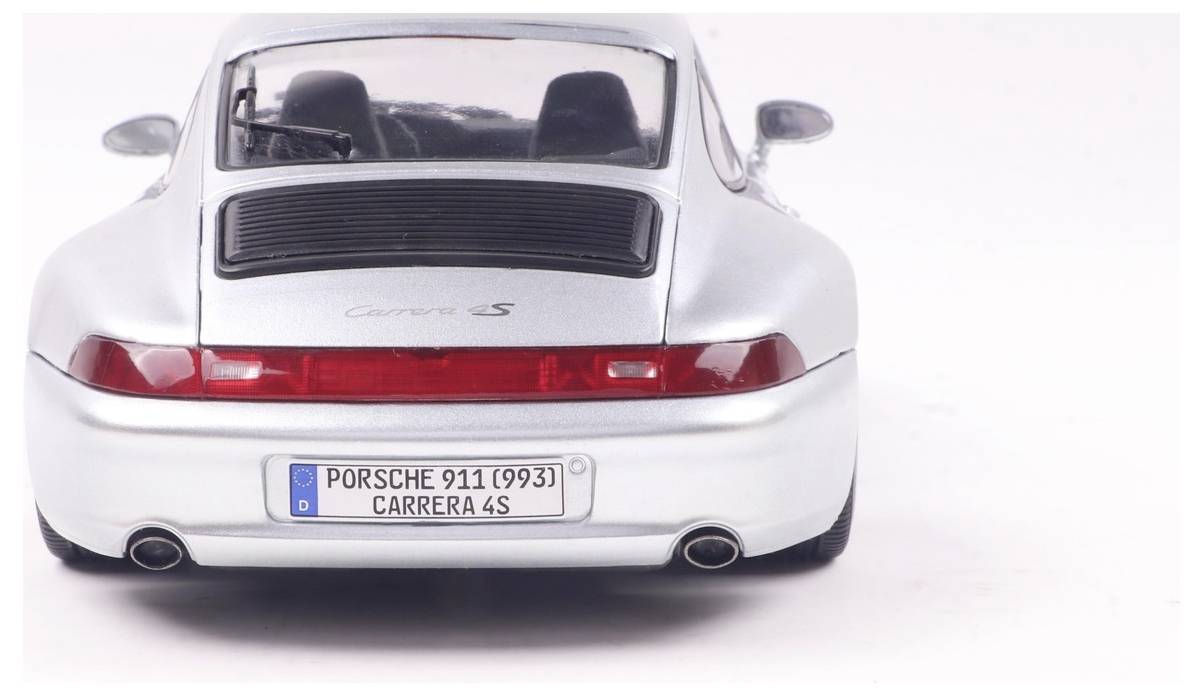 A silver Porsche Carrera 4S car model viewed from the rear, featuring a spoiler, dual exhausts, and a German license plate.