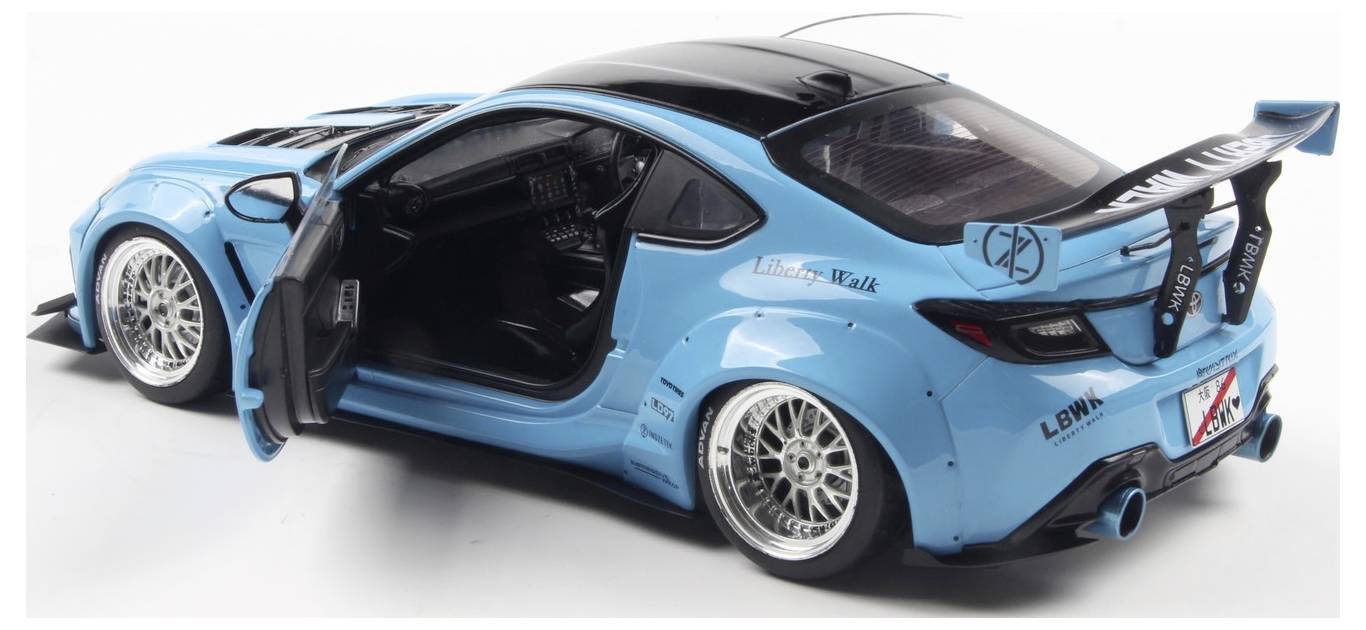 A blue sports car with doors open, featuring a large rear spoiler, wide body kit, and custom wheels. The car is parked in a studio setting.