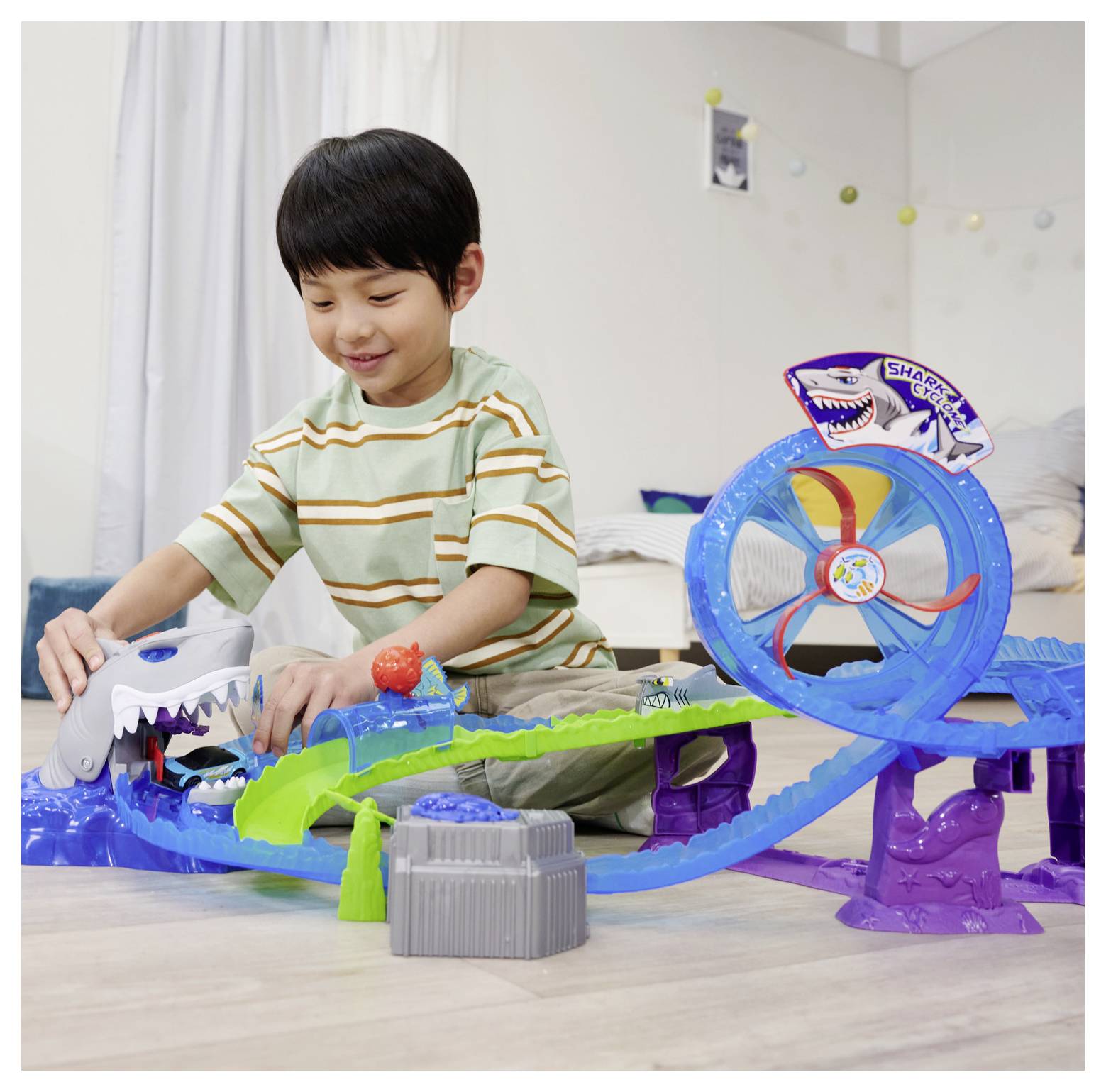 A child plays with a colorful dinosaur-themed toy track set, featuring a blue looping track and a white dinosaur head mechanism.