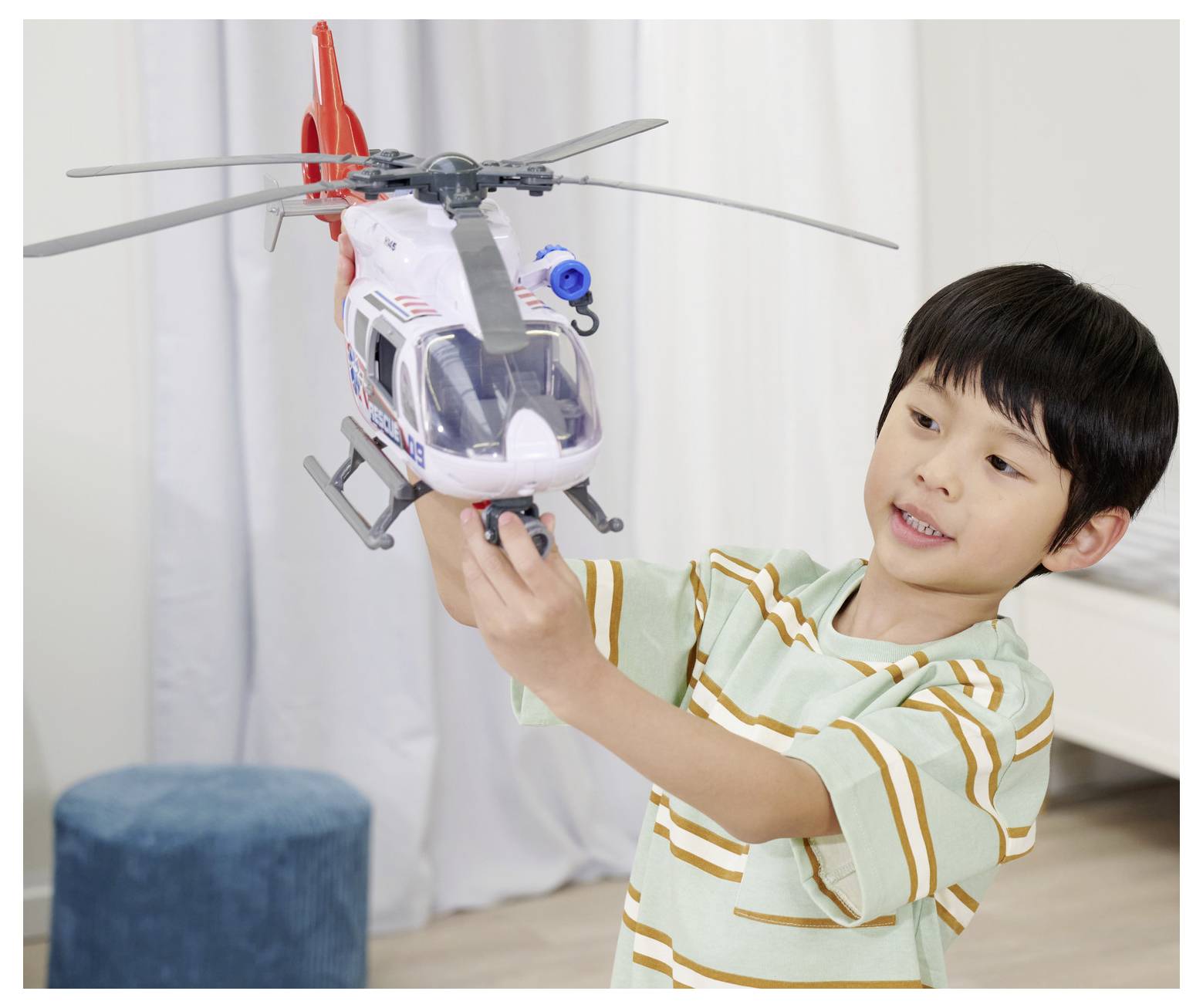 A child in a striped shirt joyfully plays with a toy helicopter indoors, suggesting a playful and imaginative moment.