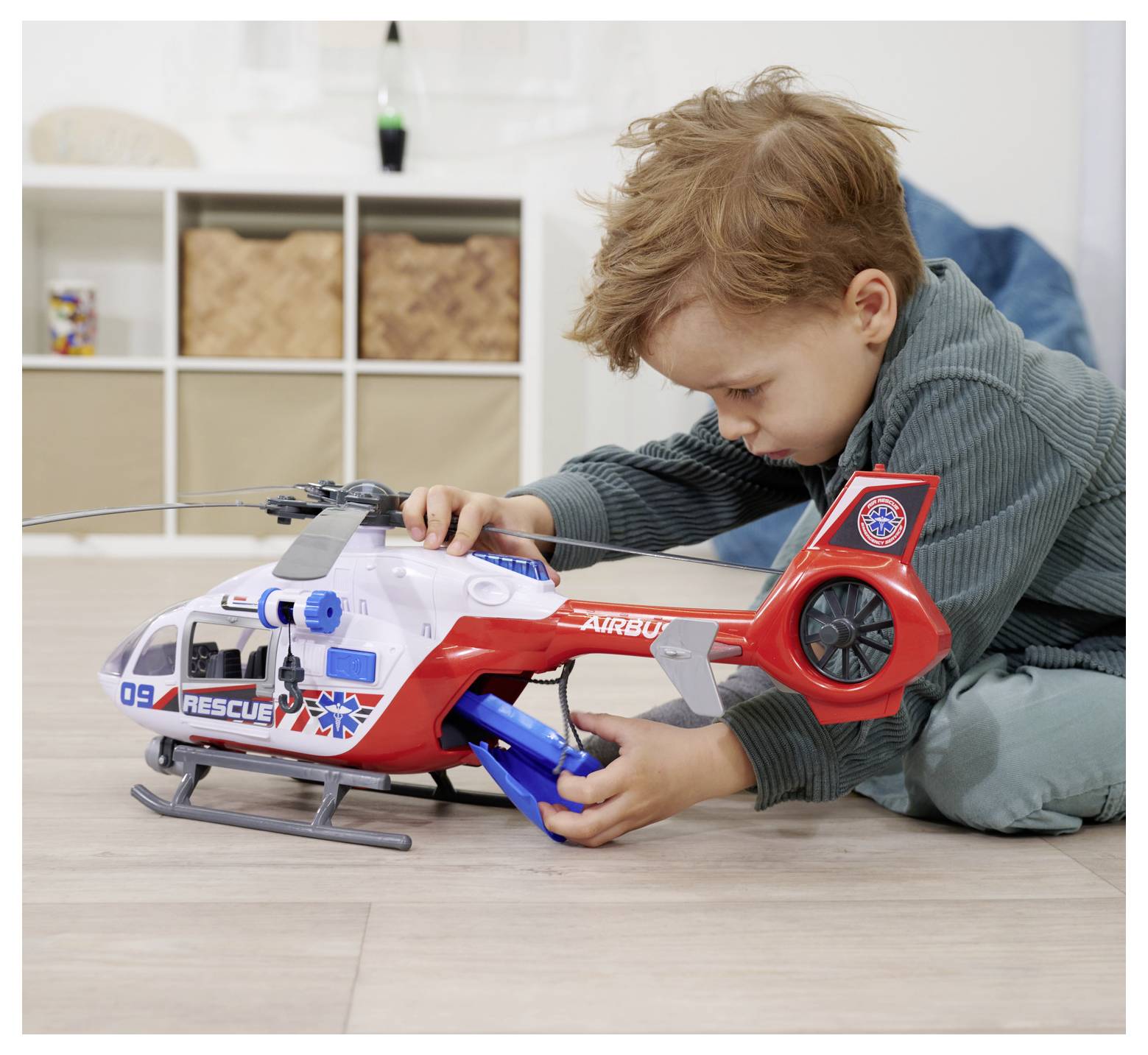 A young child playing with a brightly colored rescue-themed toy helicopter indoors, focusing intently on the toy's features.
