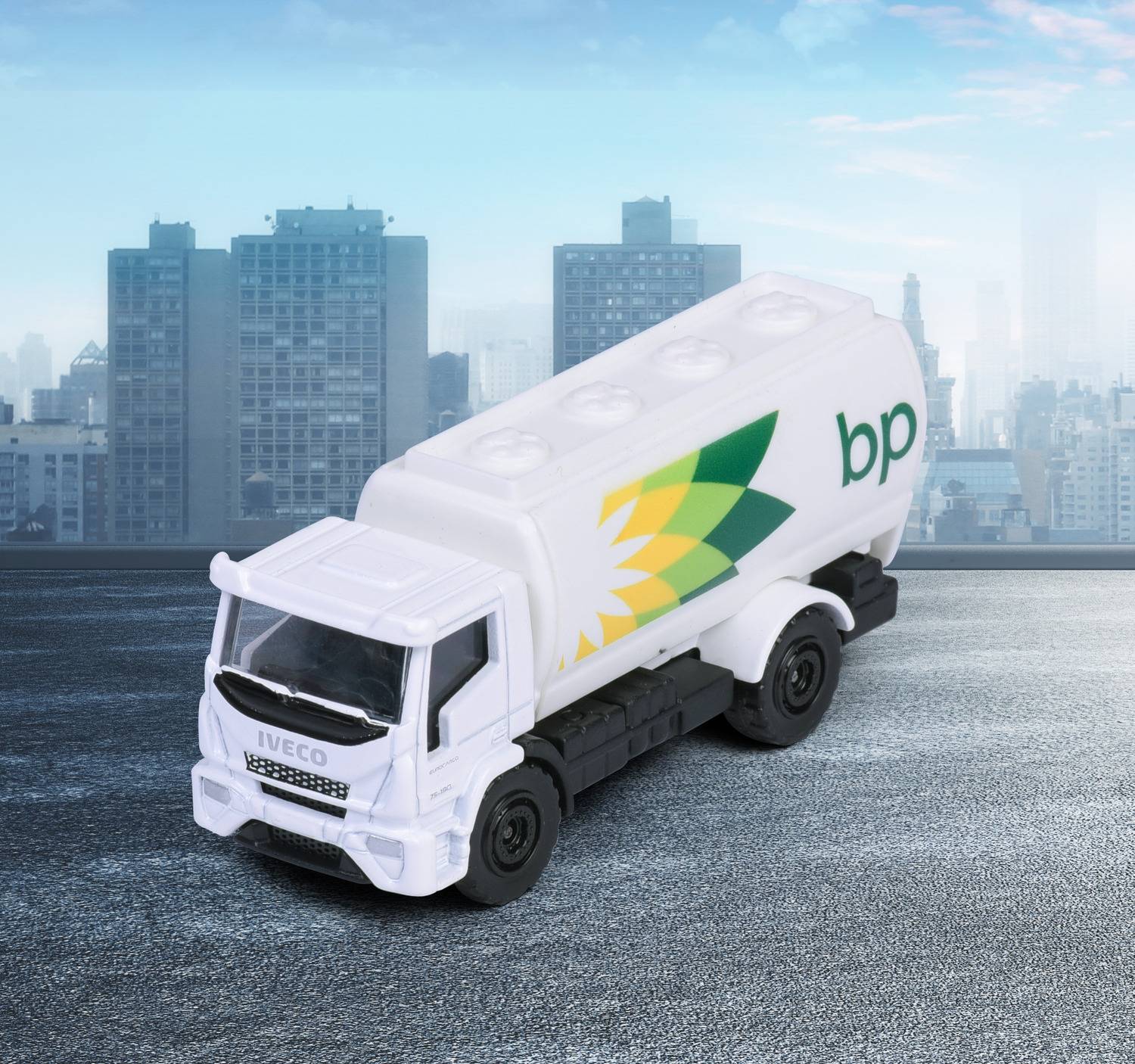 A toy fuel truck with 'bp' logo and green-yellow design is on a textured surface against a city skyline background.