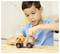 A child in a blue shirt plays with an orange toy truck at a table, smiling with focus on the toy.