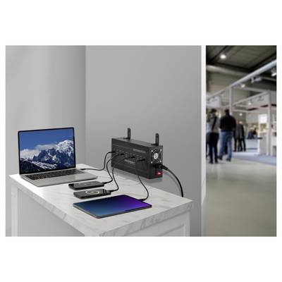 A room with devices charging on a desk: a laptop, tablet, and smartphone are plugged into a wall-mounted charging station.