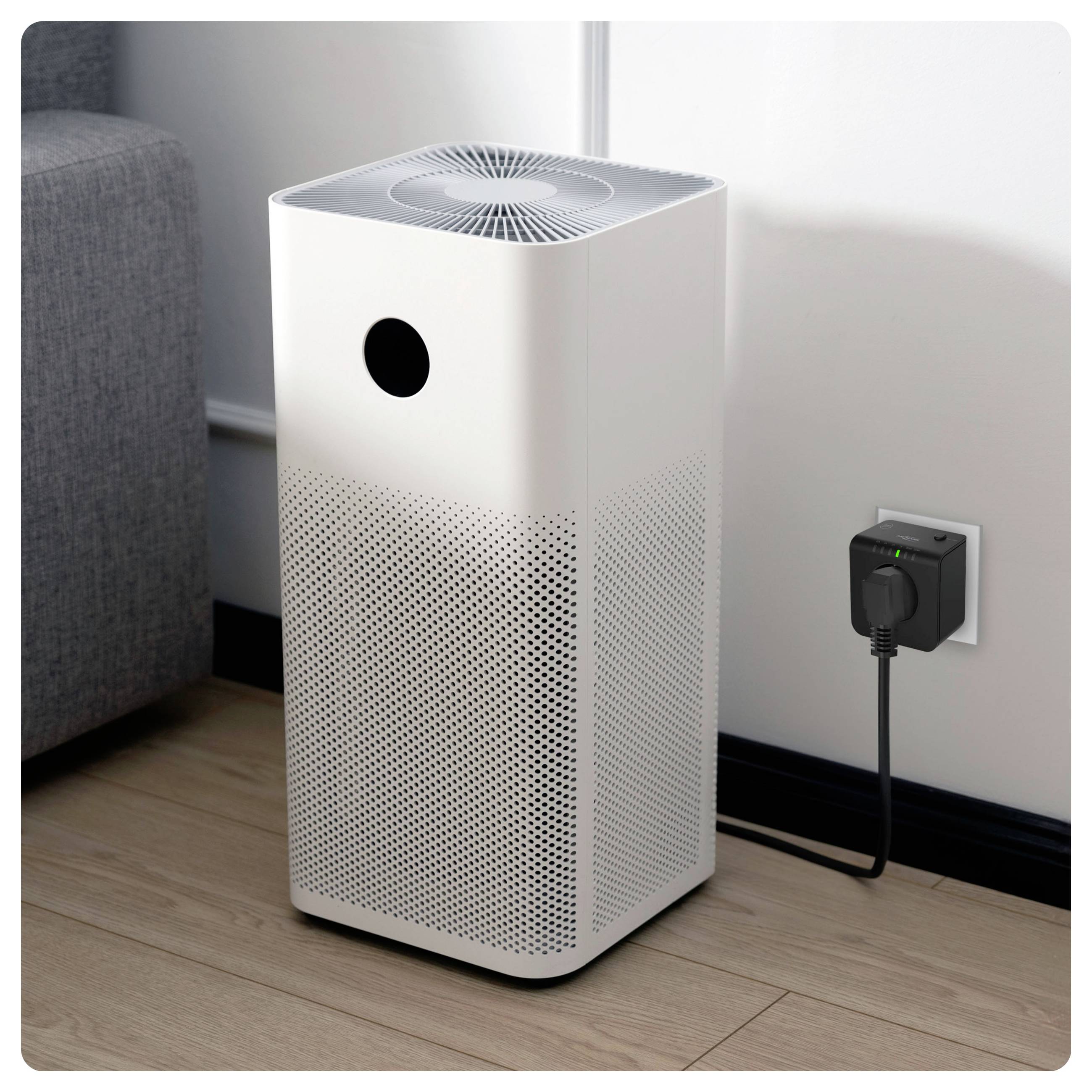 Air purifier plugged into a wall socket near a gray couch, designed for modern indoor air cleaning.