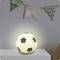 A glowing soccer ball-shaped lamp sits on a white table under a decorative flag banner.