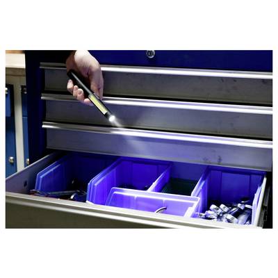 A person holds a flashlight illuminating open drawers filled with various tools in a workshop setting.
