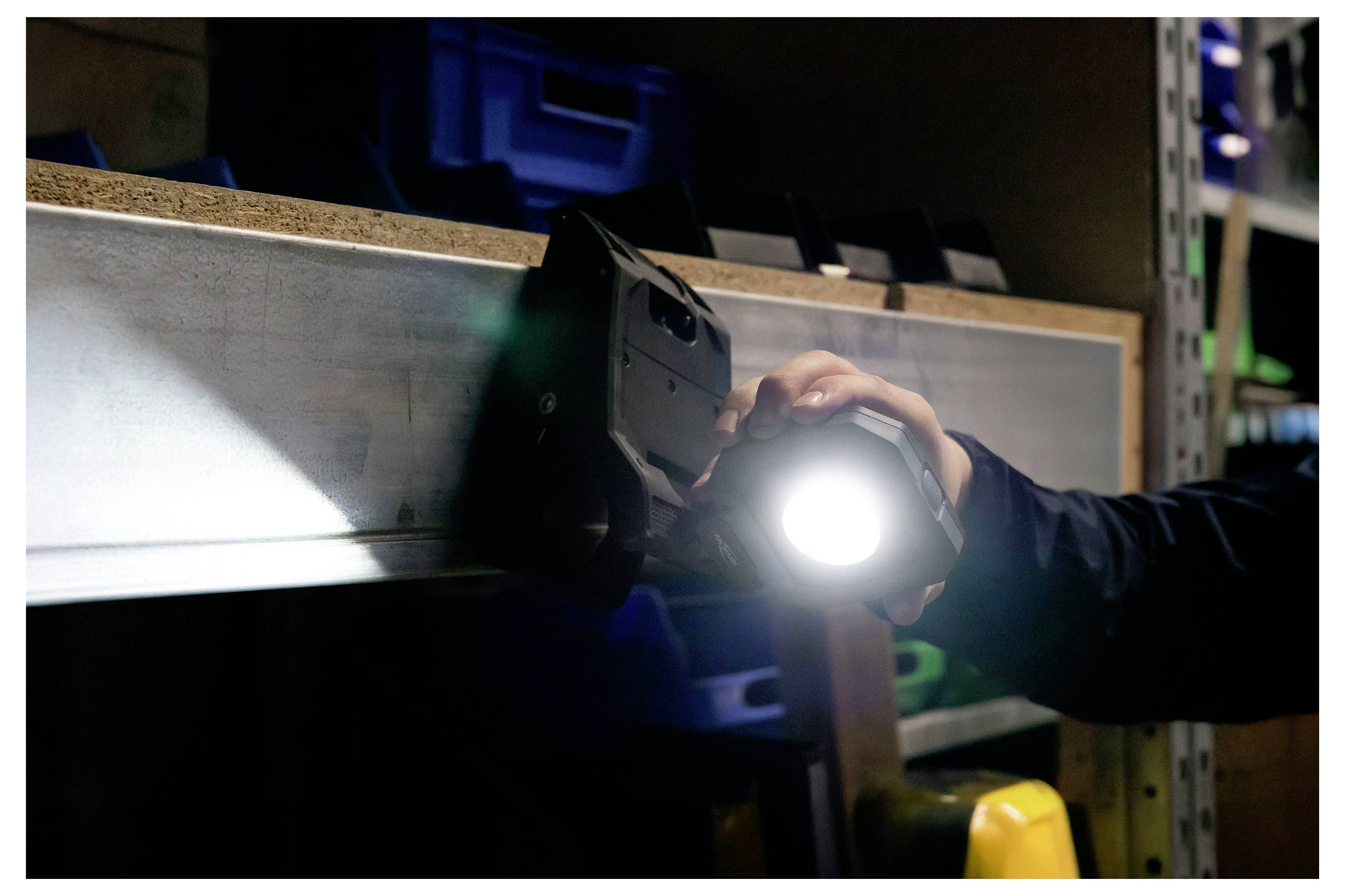 A person holds a bright flashlight in a dimly lit space, illuminating a metal shelf.