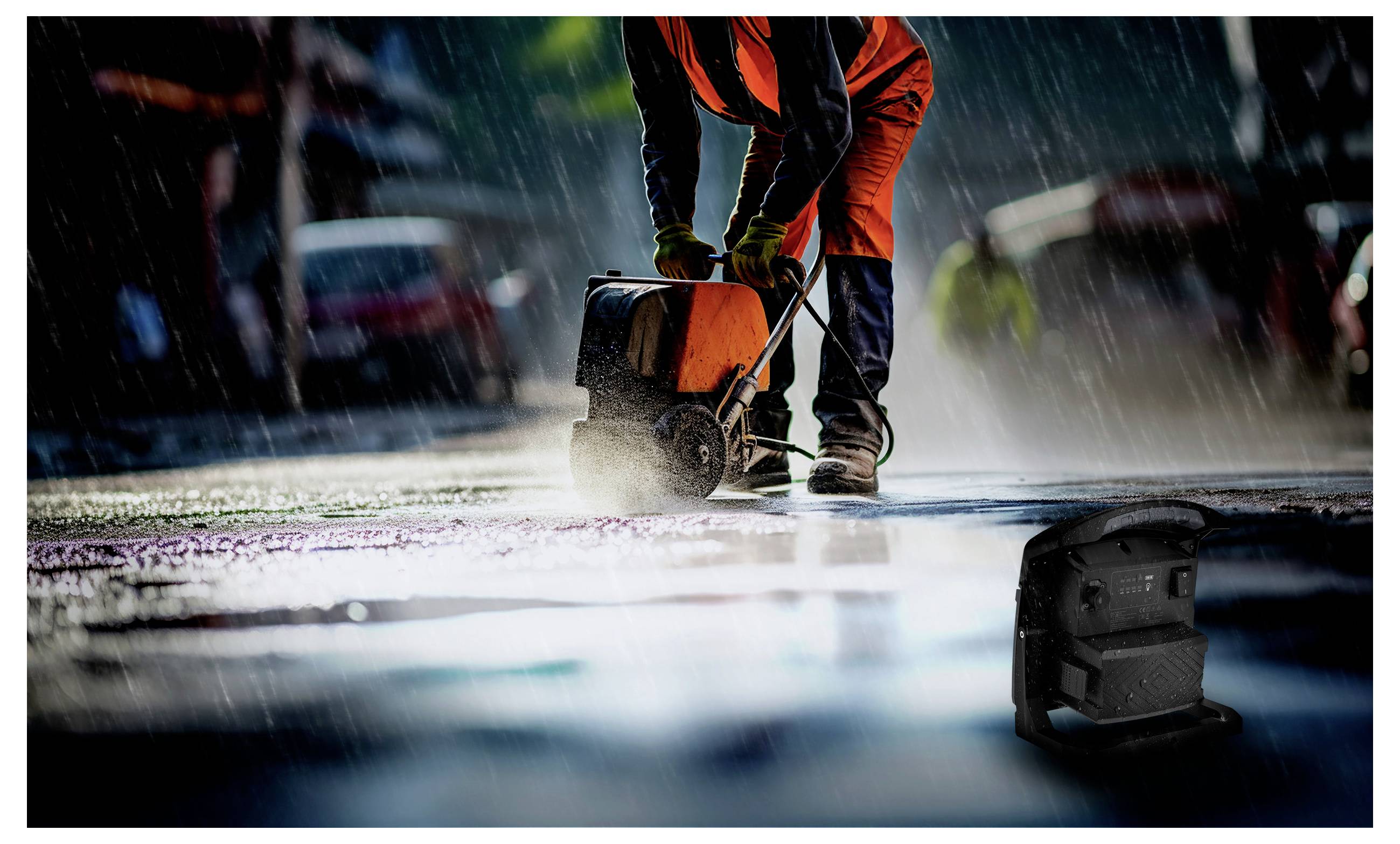 A construction worker in orange gear operates machinery on a wet road during rainfall.