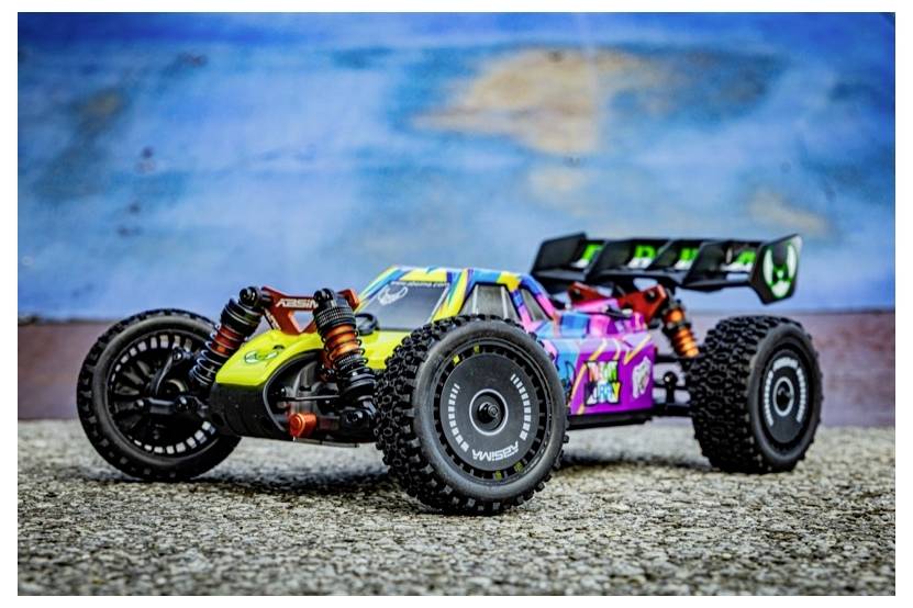 A colorful remote-controlled car with large off-road tires on a textured surface against a blurred blue and brown background.