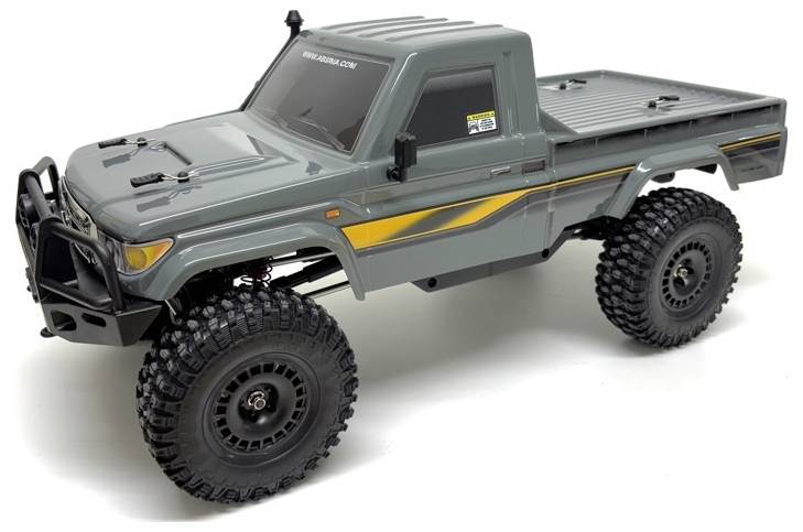 A grey remote-controlled off-road truck with large tires and a flatbed, featuring yellow stripes on the sides, on a white background.