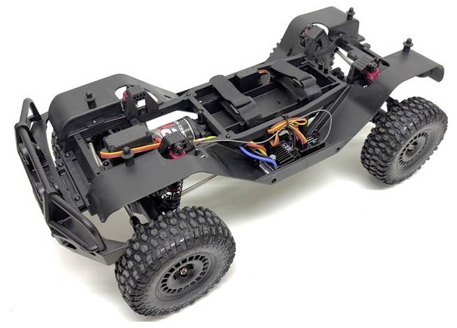 A black RC truck chassis with exposed wiring and large knobby tires, showcasing its internal structure and components.