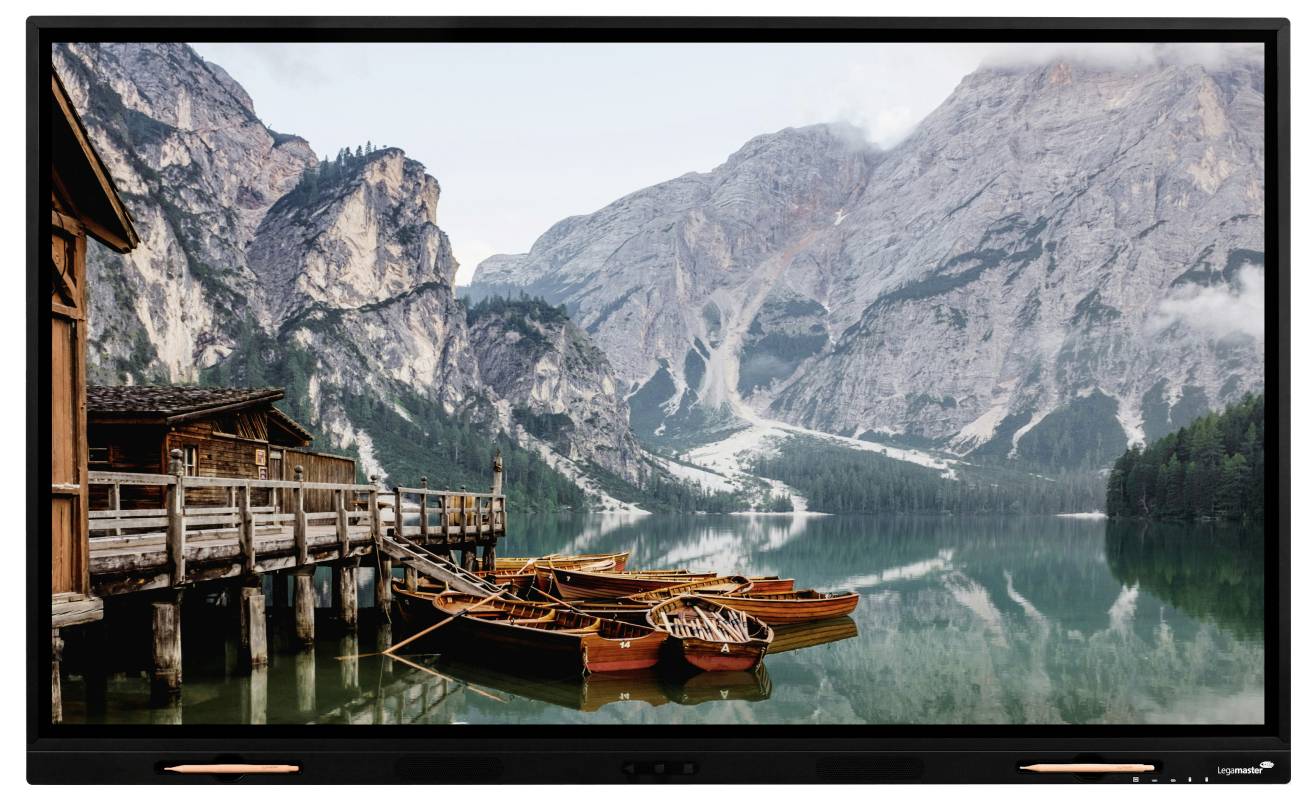A serene lake with several boats docked, bordered by a wooden pier and surrounded by majestic mountains under a cloudy sky.