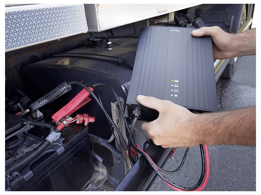A person connects a Cytek battery charger to a vehicle battery, showing the usage process outdoors.