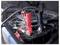 A close-up of a car battery with red and black jumper cables attached, indicating a jump-start or battery charging process.