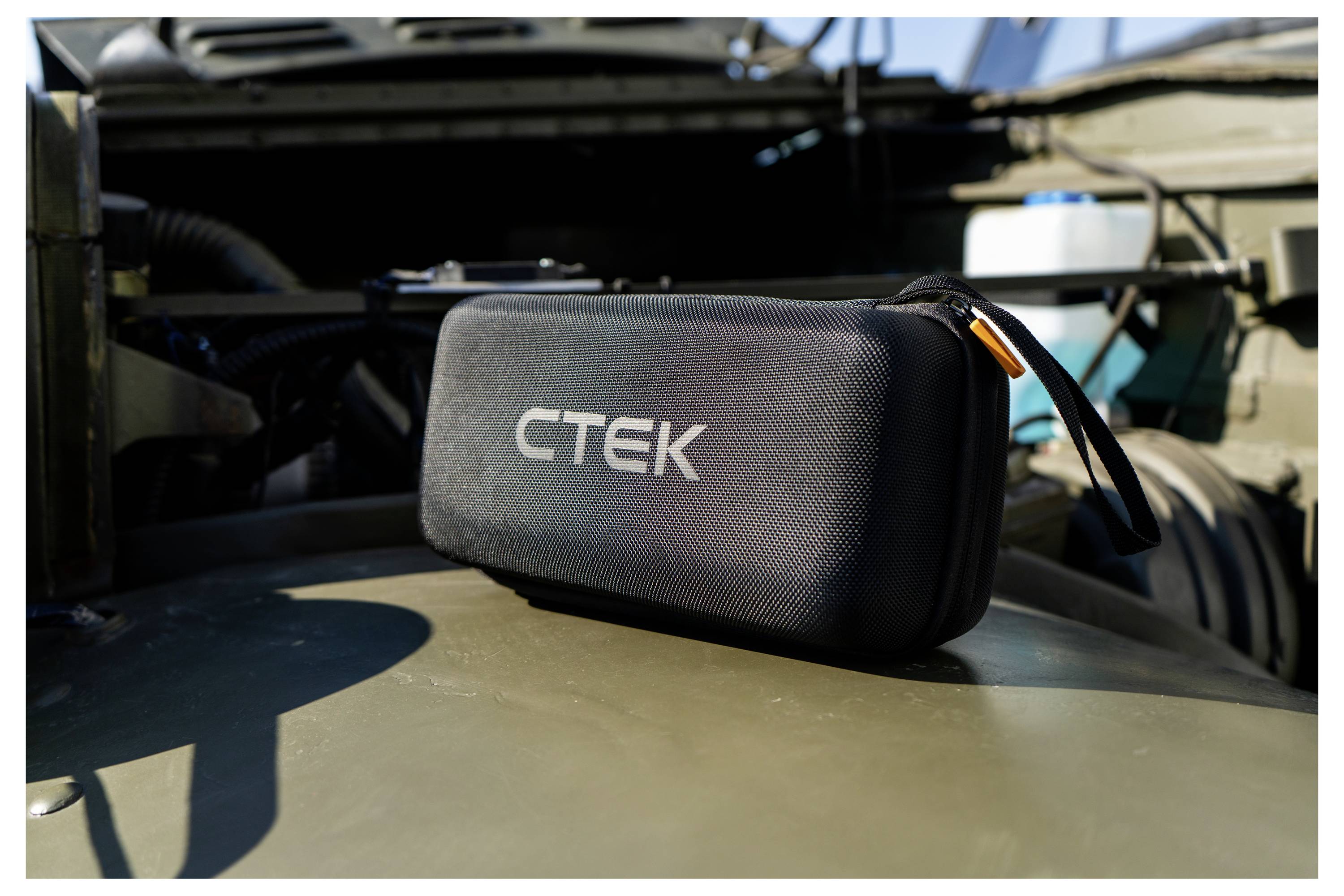 A black CTEK-branded carrying case is placed on a military vehicle hood in a sunlit outdoor setting.