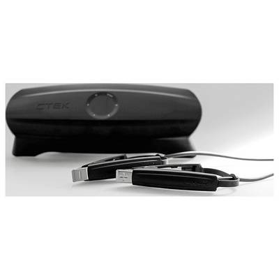 Black CTEK battery charger with attached clamps lies on a white surface, emphasizing a sleek design and practical functionality for vehicle charging.
