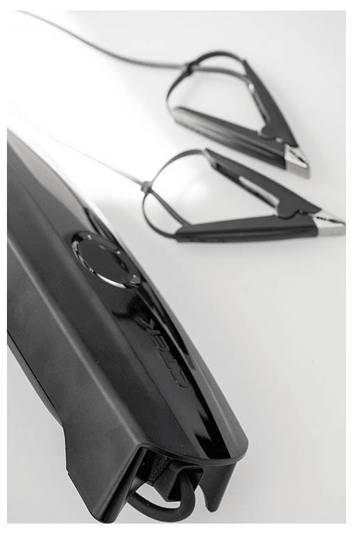 A black car jump starter with attached alligator clamps is positioned diagonally on a white surface. The device has a sleek design.