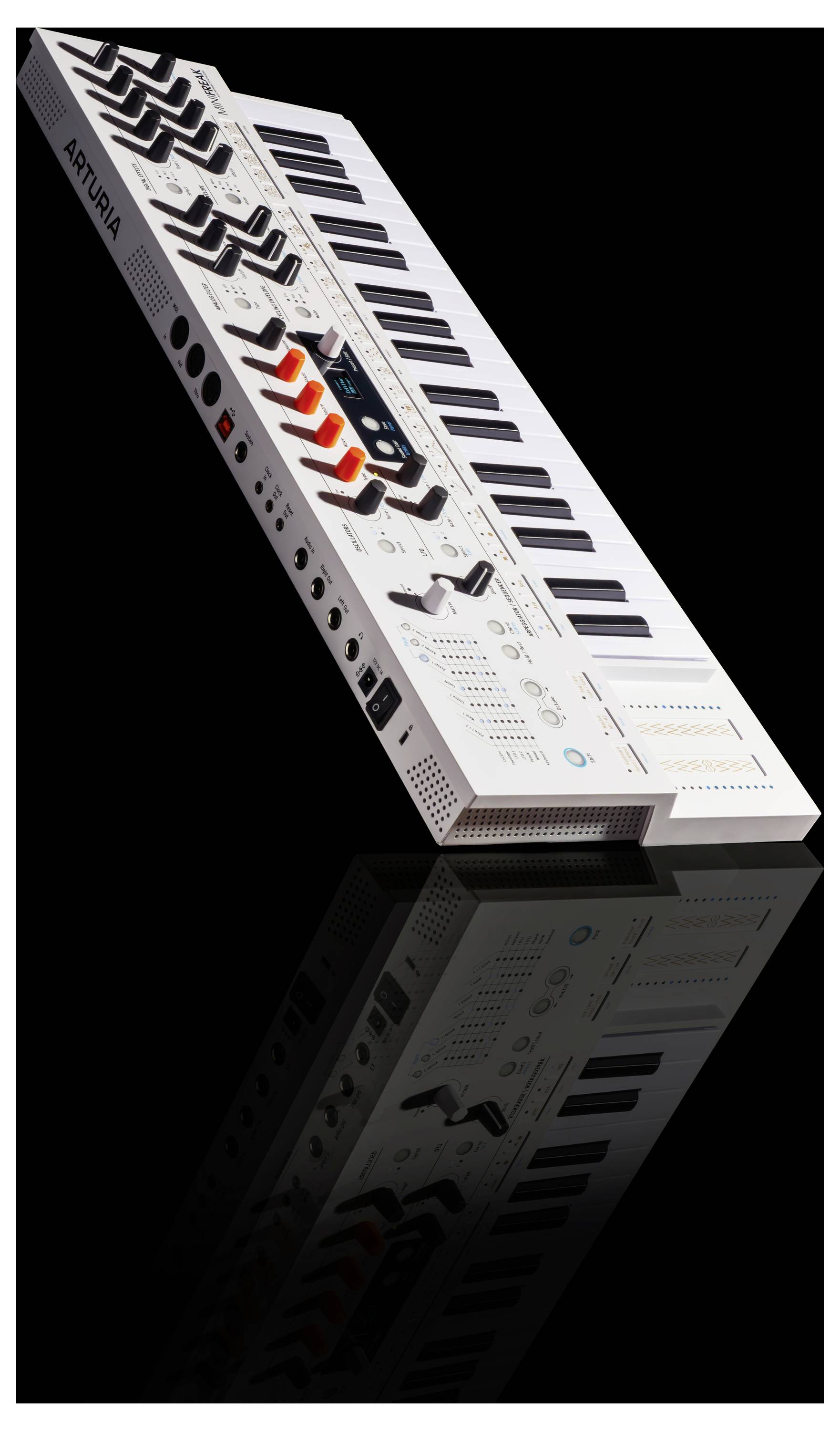A white synthesizer keyboard with black keys and various colored knobs is angled on a reflective black surface.
