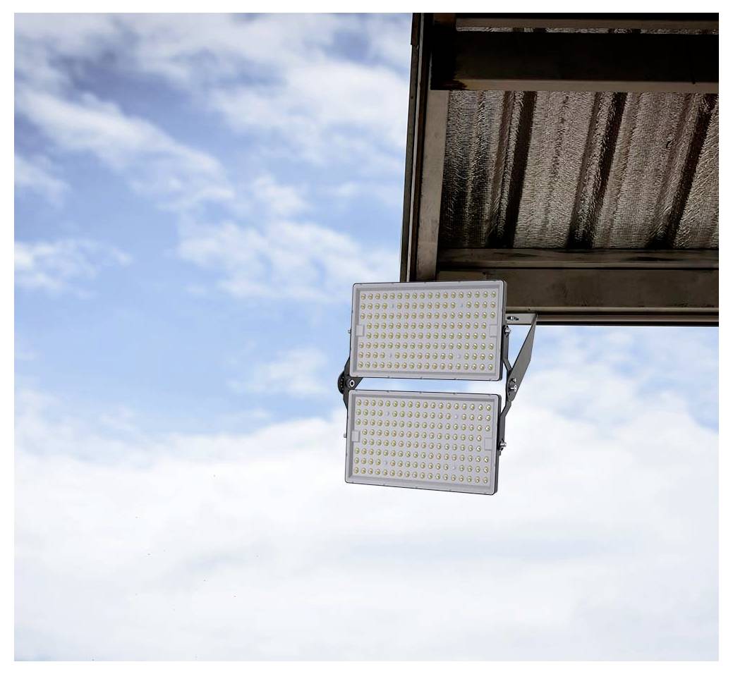 Outdoor LED light fixture mounted on a building under a cloudy blue sky, providing energy-efficient illumination for the area below.