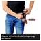 A person wearing jeans is holding a drill and securing it to their belt with a clip for convenient temporary storage.