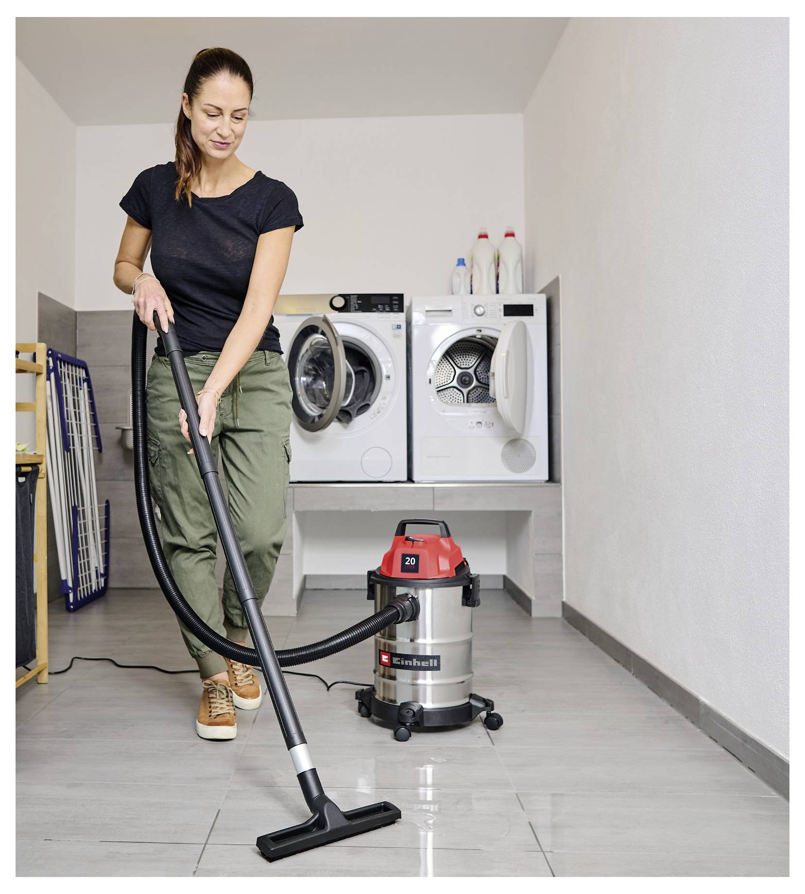 A woman vacuuming a laundry room with a red and silver vacuum cleaner; a washing machine and dryer are in the background.