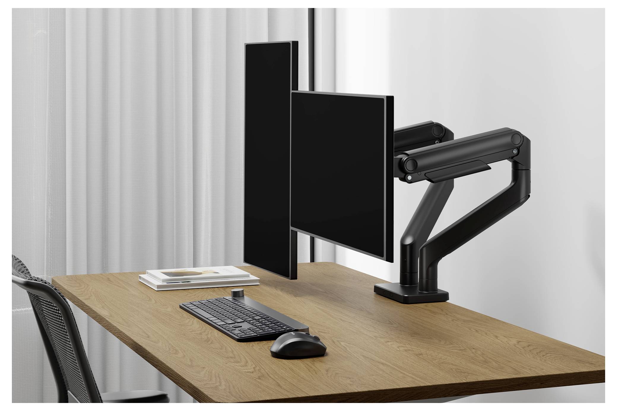 'An ergonomic dual-monitor setup on a wooden desk with an adjustable arm, keyboard, mouse, and stacked notepads, near a window.'