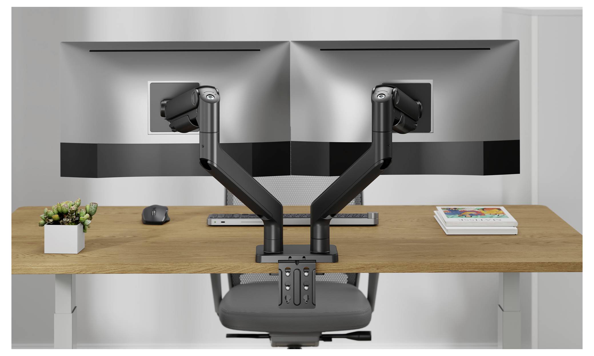 A modern office desk with dual monitors mounted on adjustable arms, a keyboard, mouse, a plant, and a book, viewed from the front.