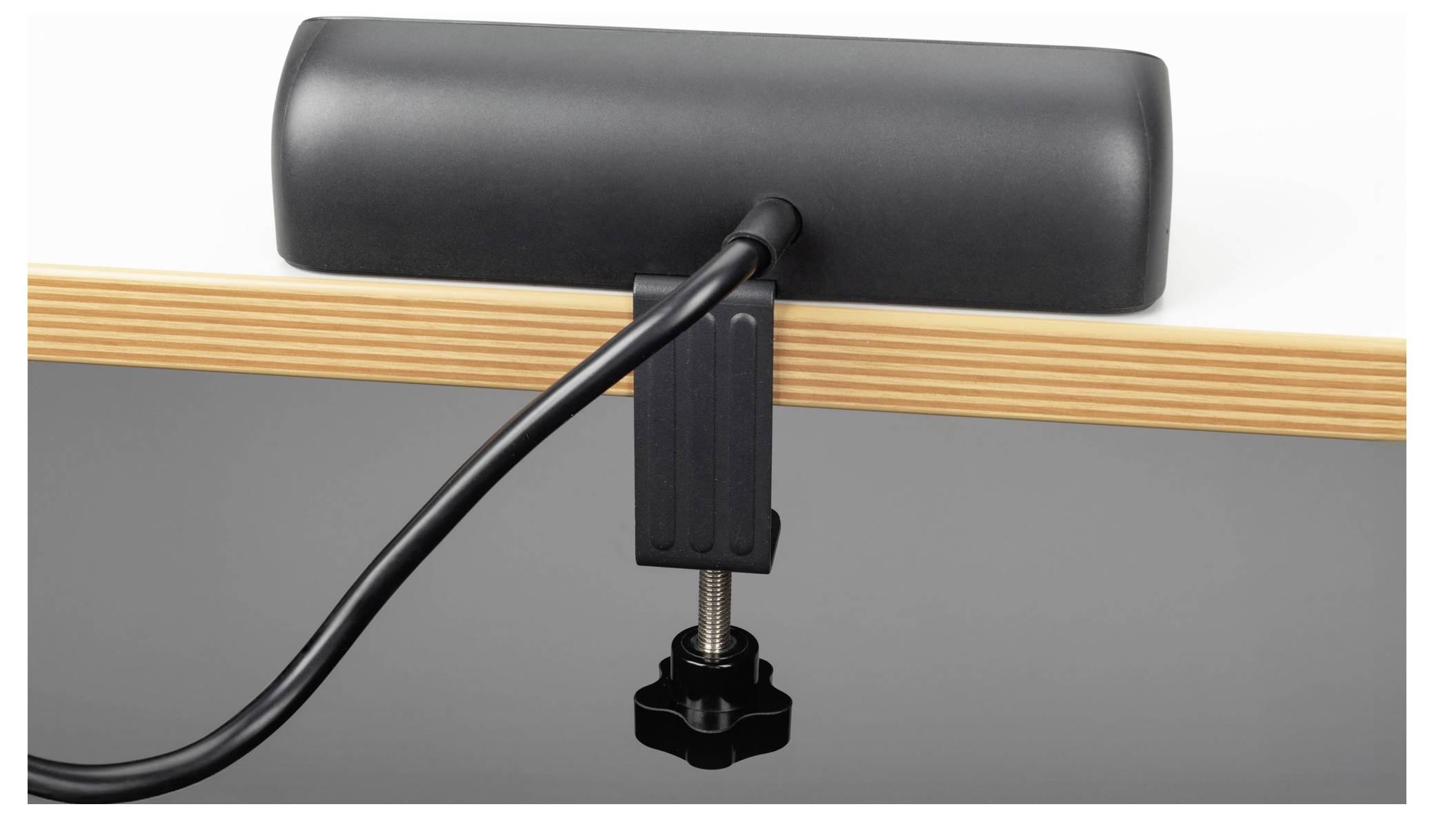 A black desk lamp with a clamp attaches to a table edge, with a cord trailing from it.