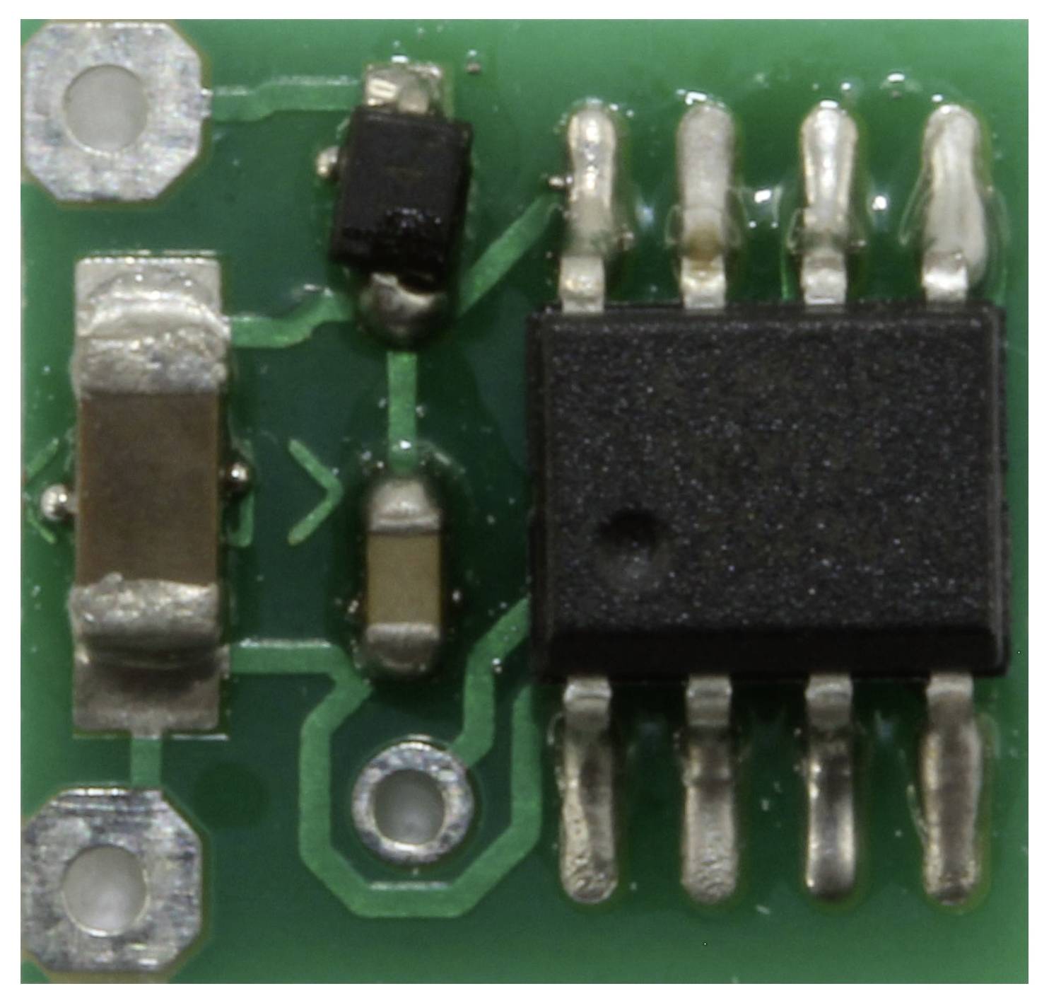 A small green circuit board with multiple soldered components, including a black rectangular chip with four pins on each side.