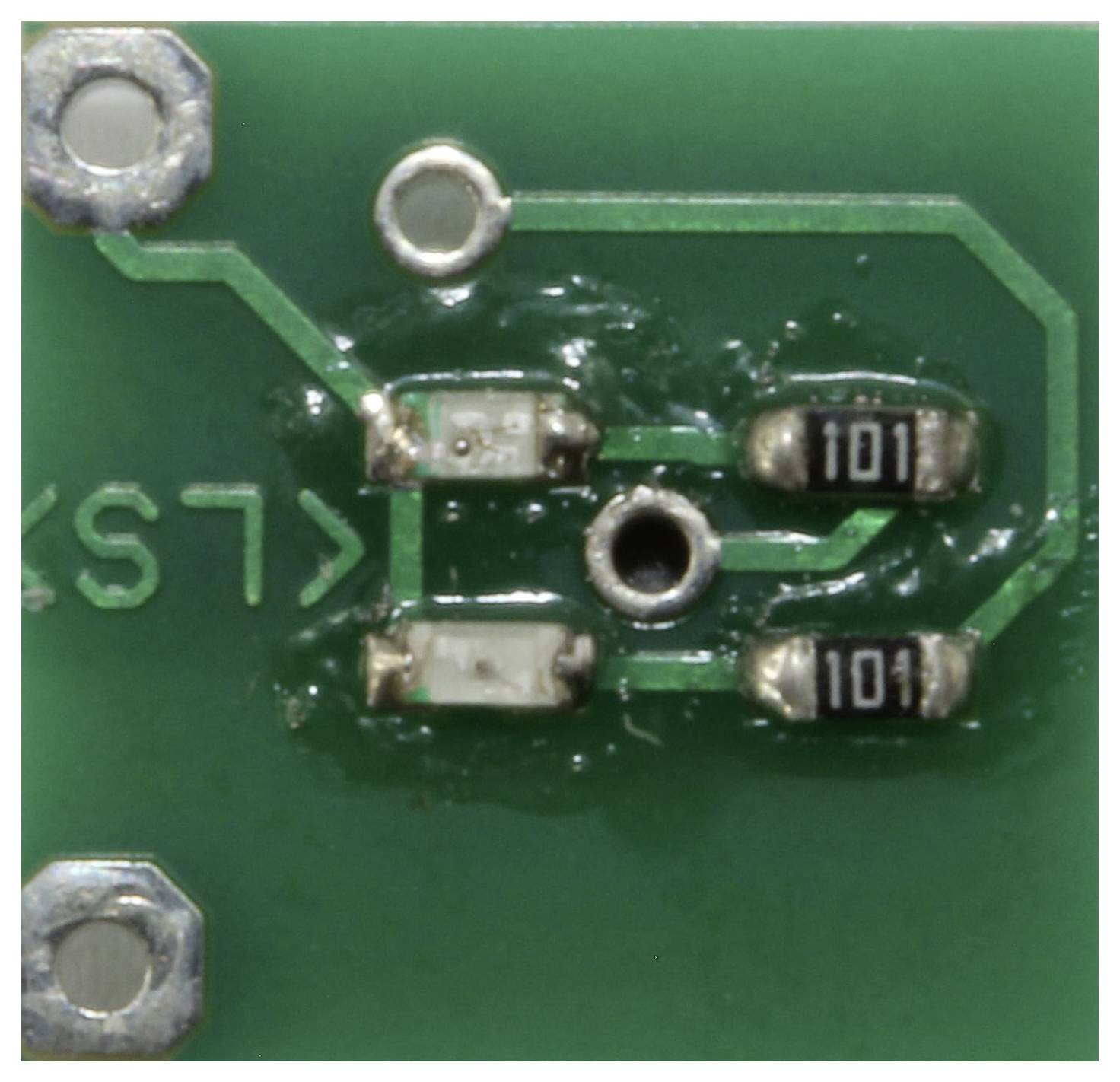 Close-up of a green circuit board featuring two small resistors labeled '101'. The board has metallic connections and soldering points.
