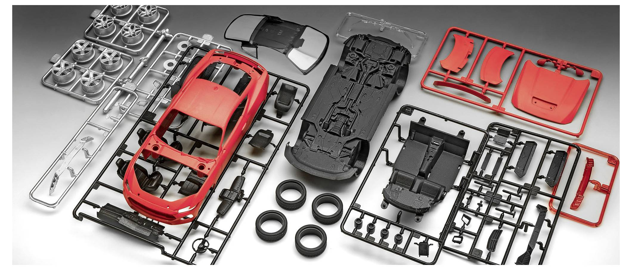 Model car kit with disassembled parts including wheels, body, and chassis, arranged on a gray surface.