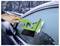 A hand uses a green ice scraper to clear frost from a car window on a snowy, winter road.