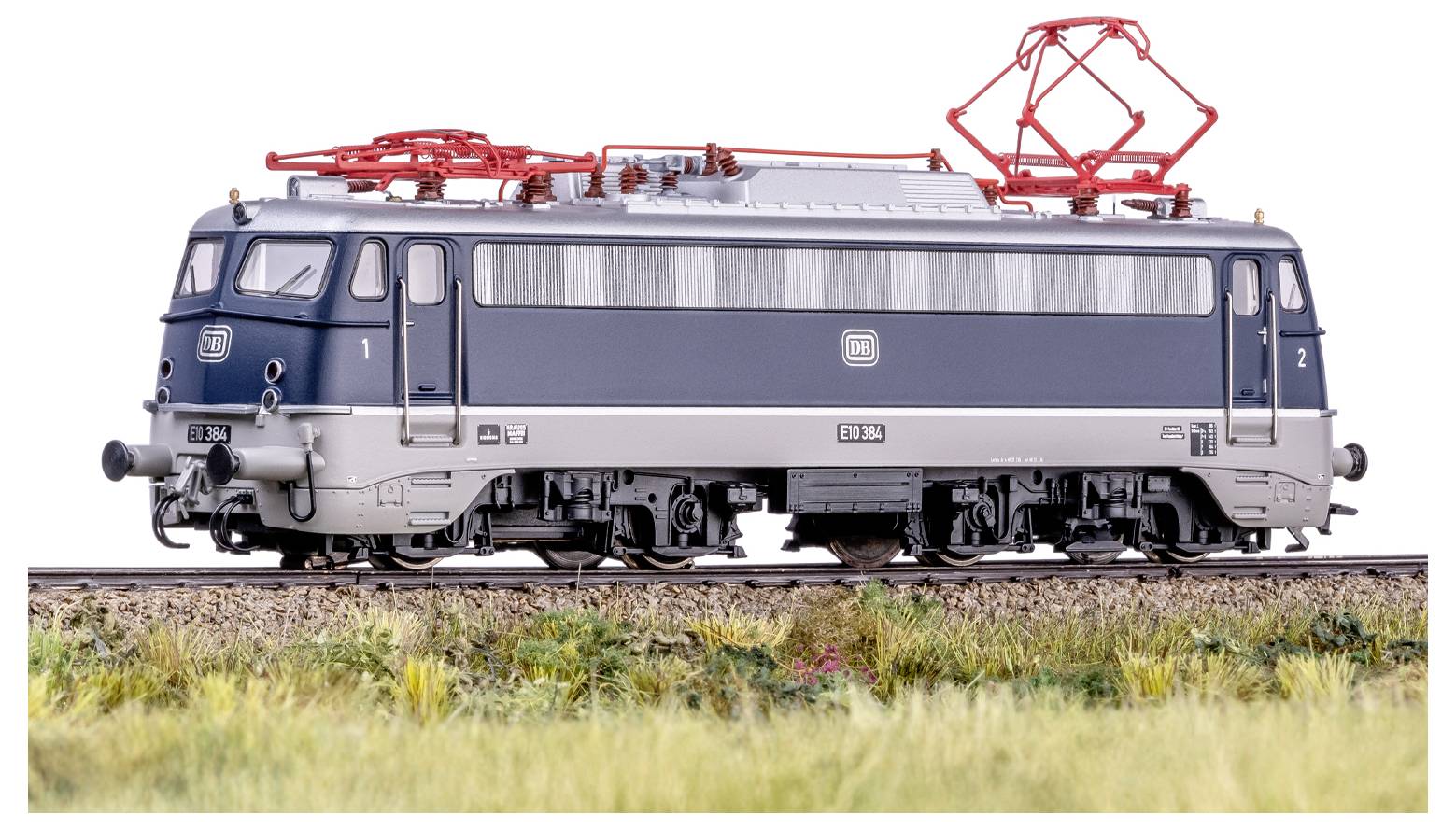 A model train locomotive on a track with a grassy landscape, showcasing intricate details like red overhead wires and a two-tone color scheme.
