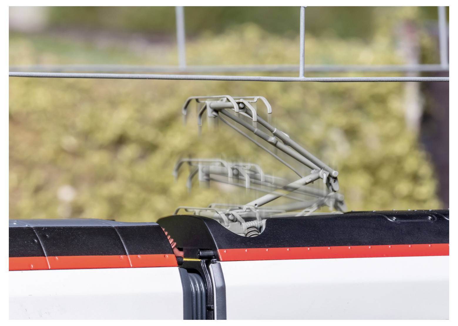 A high-speed train roof with a blurred pantograph indicating motion against a blurred background of greenery.