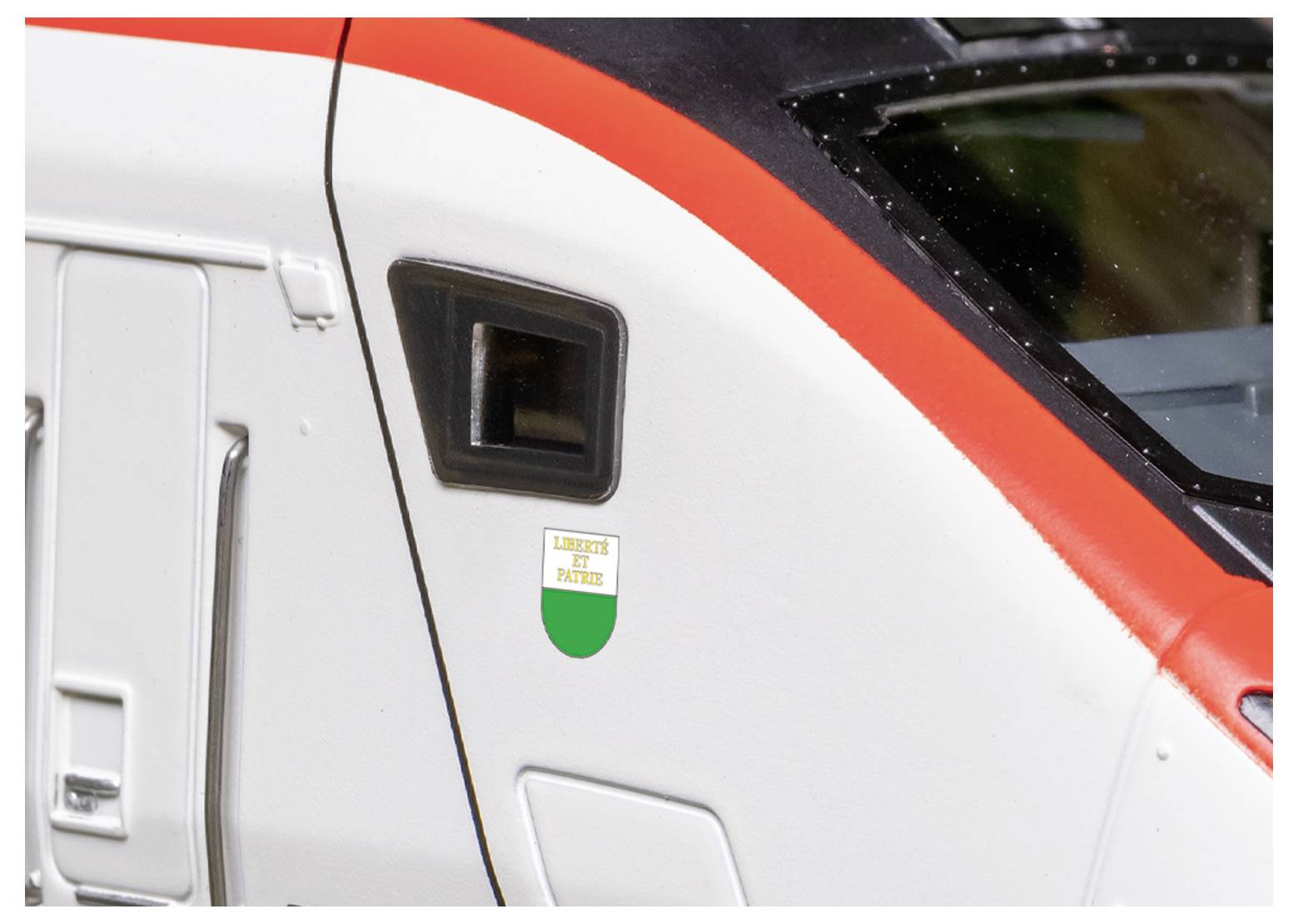 A close-up of a train door with a red and white exterior, featuring a small Italian shield emblem that reads 'Liguria di Ponente'.