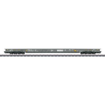 A long, grey flatbed rail car with multiple wheels is displayed, showing various labels and symbols along its side. It stands on tracks.