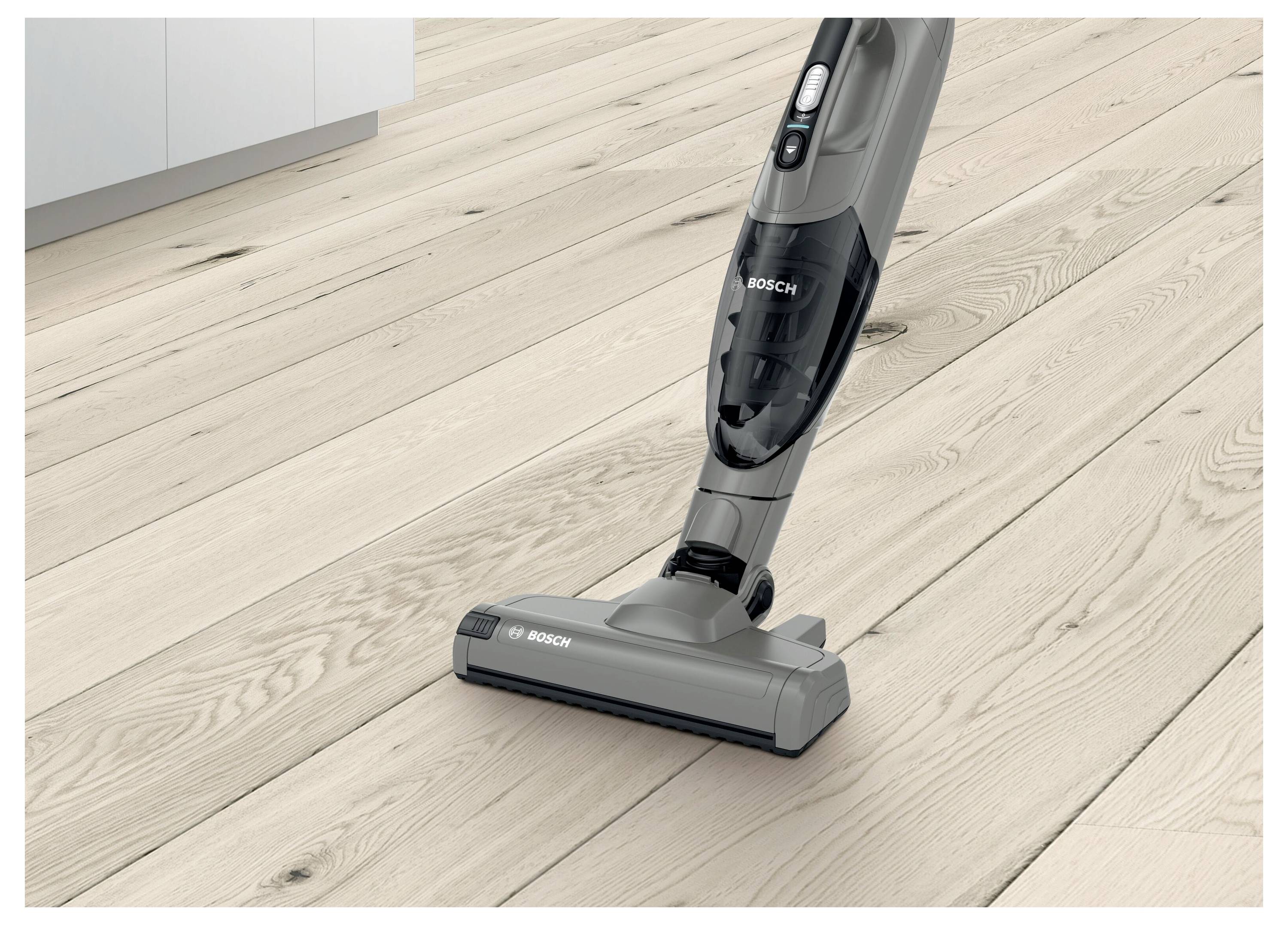 A cordless vacuum cleaner on a wooden floor near a kitchen cabinet, showcasing its mobility and suitability for cleaning hard surfaces.