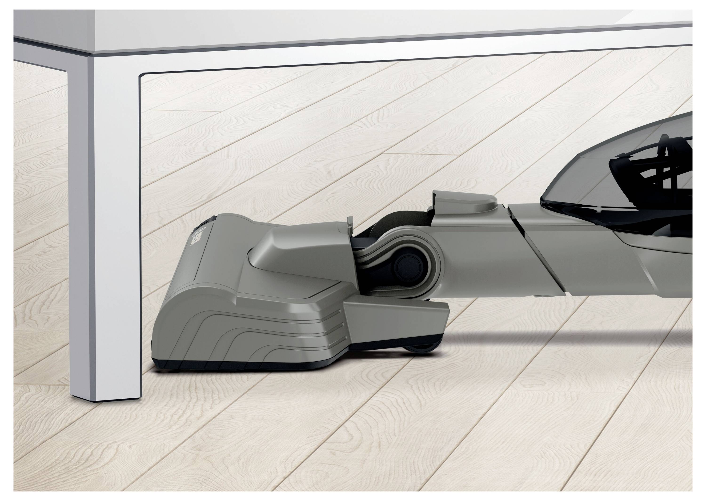 A vacuum cleaner's nozzle cleaning under a low table, highlighting its slim design for reaching tight spaces. Floorboards are visible.