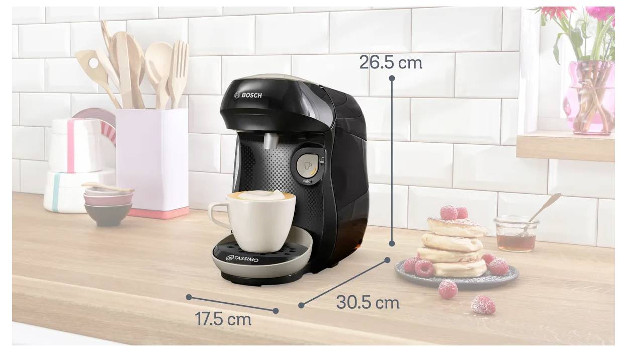 Coffee machine on a kitchen counter next to pancakes and a pink vase with flowers. Measurements shown: 26.5 cm height, 30.5 cm width, 17.5 cm depth.