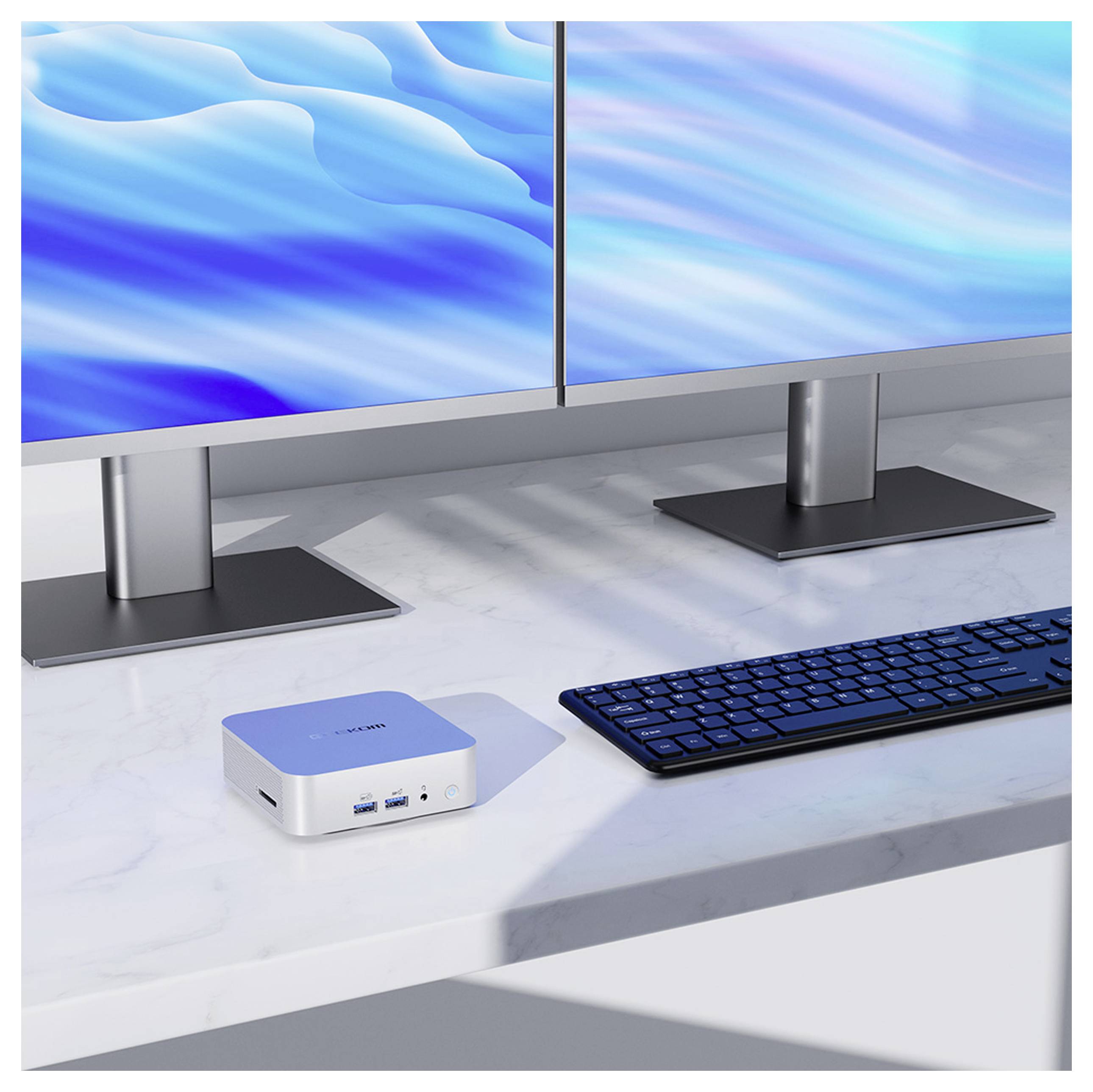 A minimalist desk setup with a compact silver computer, a black keyboard, and dual monitors displaying blue wavy patterns.