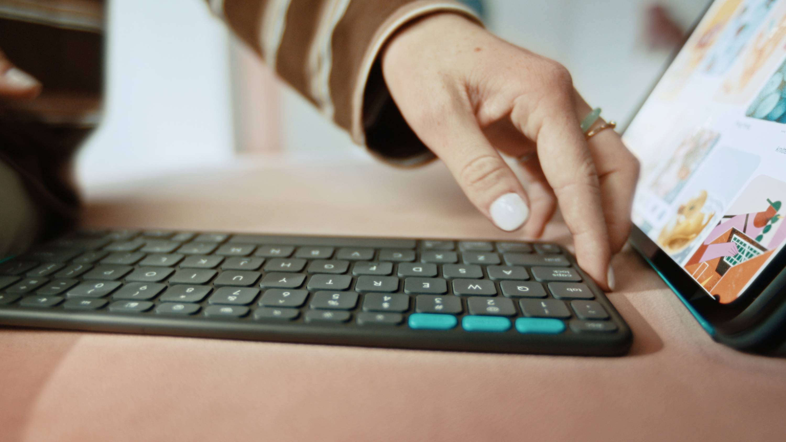 A person typing on a wireless keyboard connected to a tablet displaying colorful images, suggesting a work or creative setup.