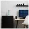 A minimalist home office with a desk, chair, monitor displaying weather data, digital clock with icons, and camera lenses on a shelf.