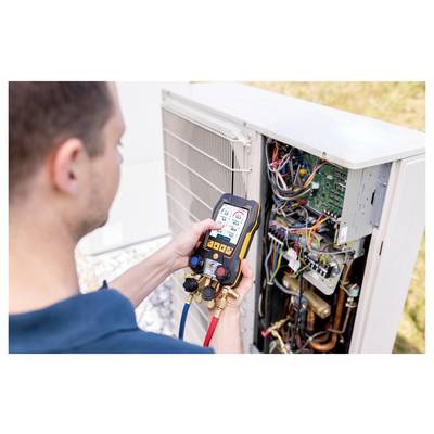 A person uses a digital multimeter to check the settings on an open and wired outdoor air conditioning unit.