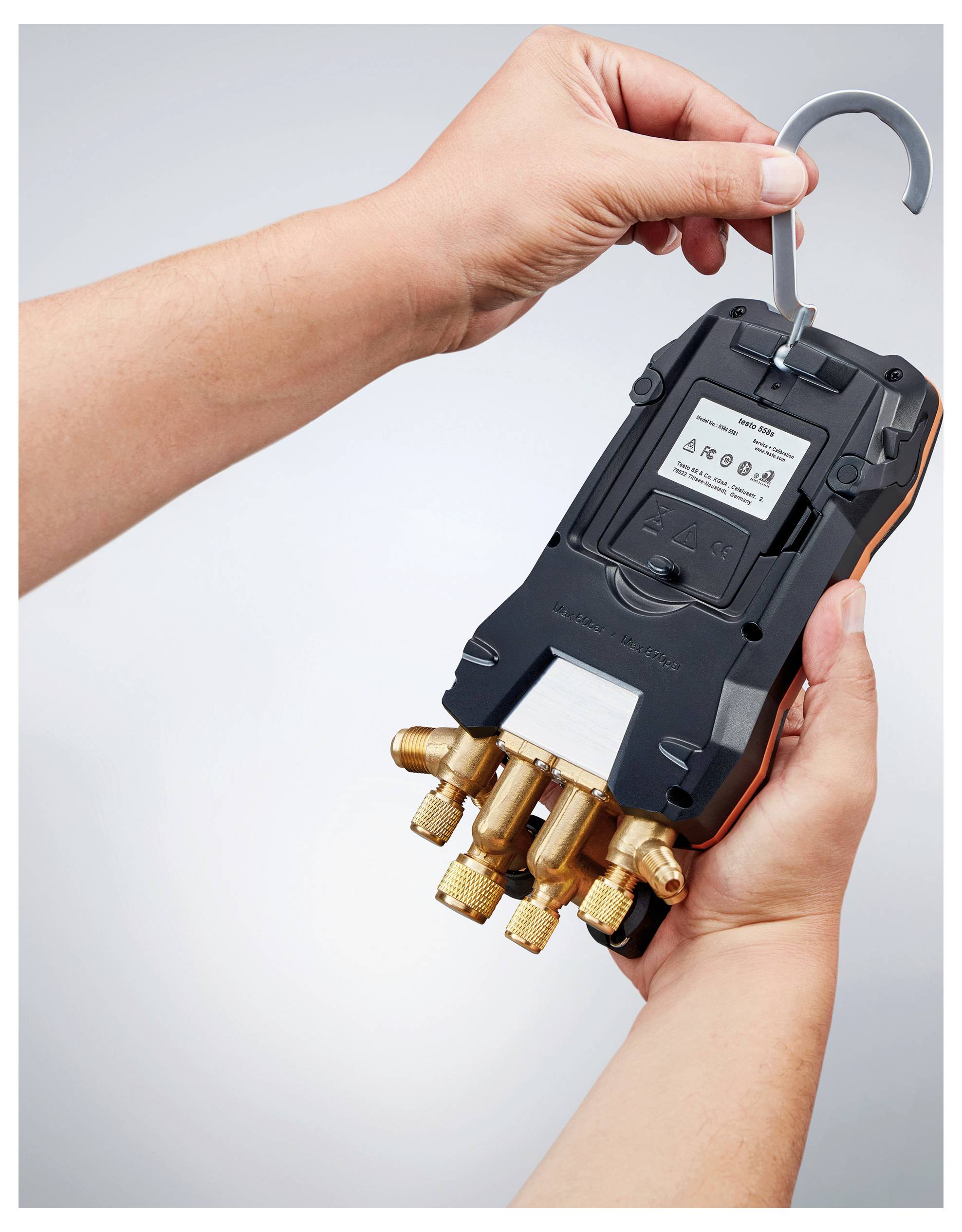 A person holds a black device with brass fittings, reading 'Smart Service Tool' on the display, used for technical measurements.