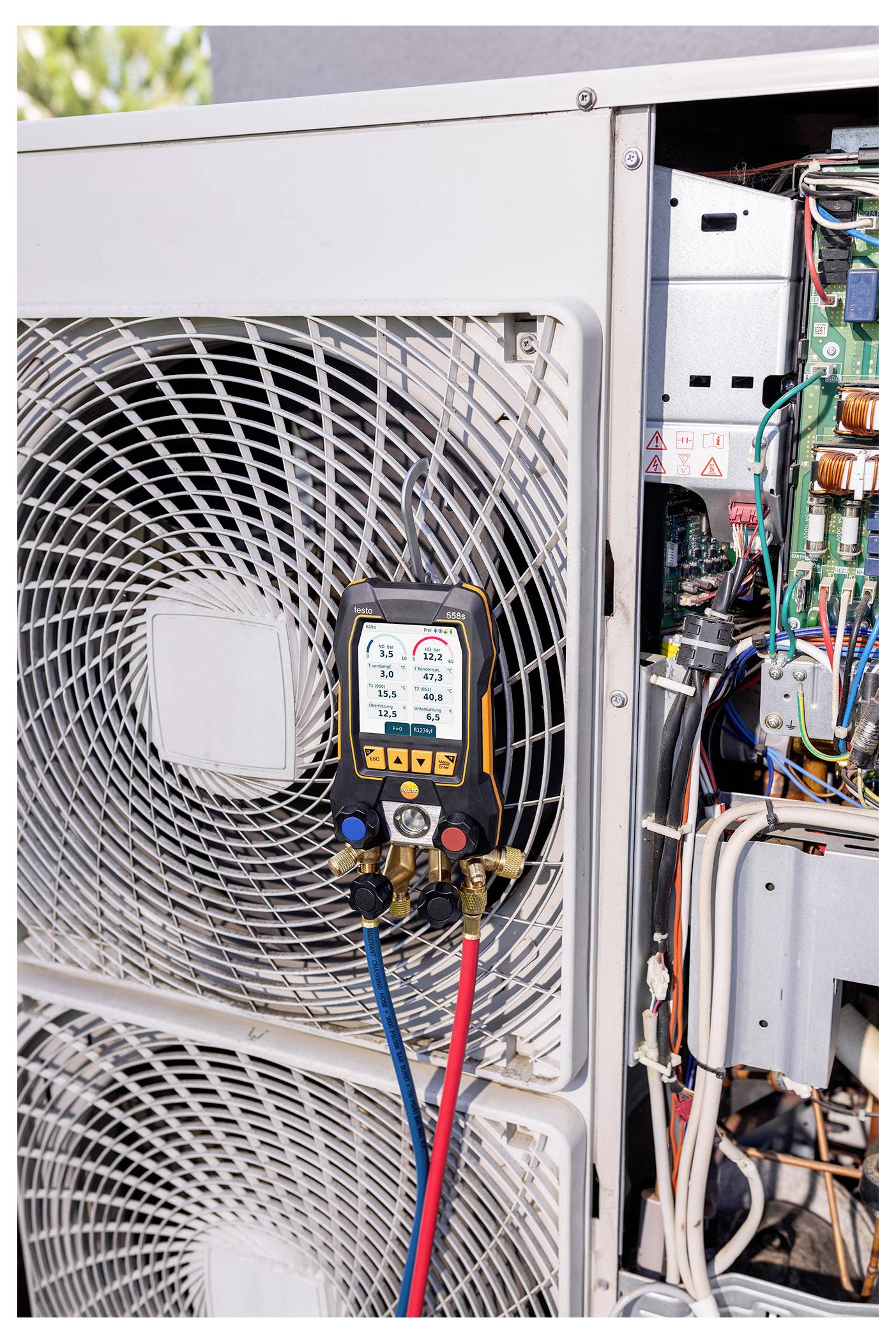 An HVAC unit is being serviced, showing a digital gauge connected to it with colorful wires. The unit's internal components are visible.